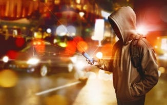 Hacker anonymous using smartphone on the street at night