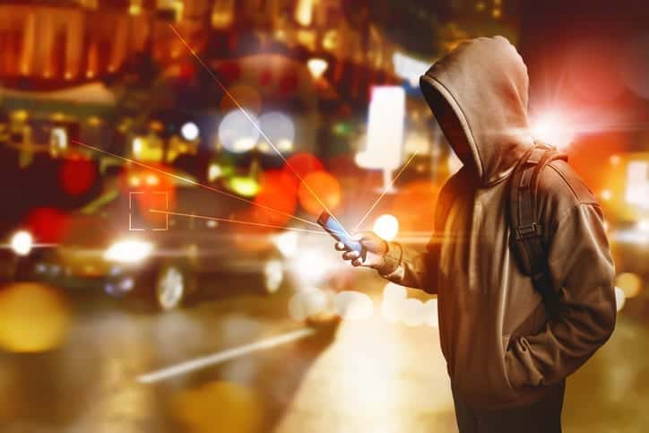 Hacker anonymous using smartphone on the street at night