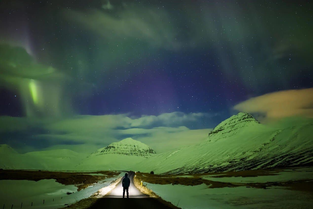 Photo of a person under northern lights in mountains