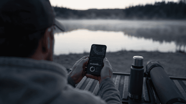 Person checking Fishbox fishing app by lake